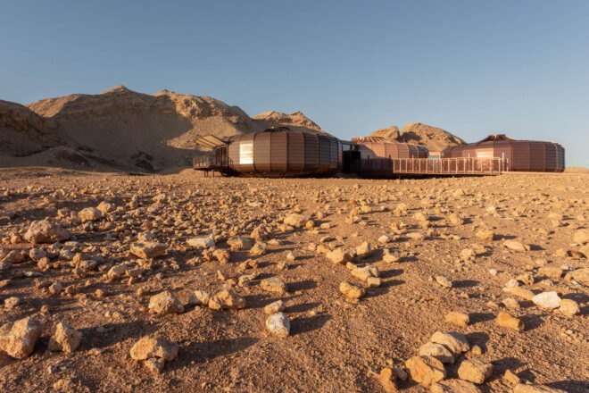 a ground angle of a desert landscape full of rocks with a dark brownish building composed of three structures