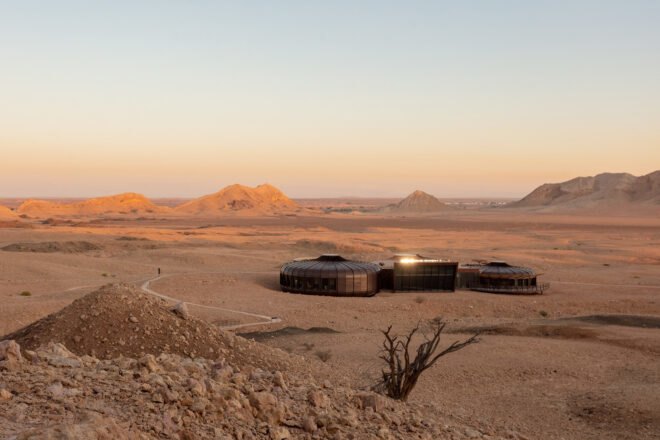 a desert landscape with a dark building composed of three structures