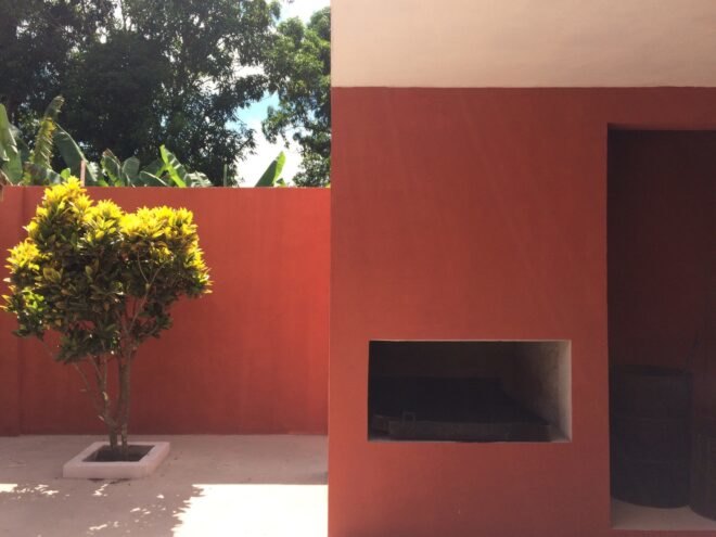 to the left, a tree, to the right a red wall with a rectangular cut-out