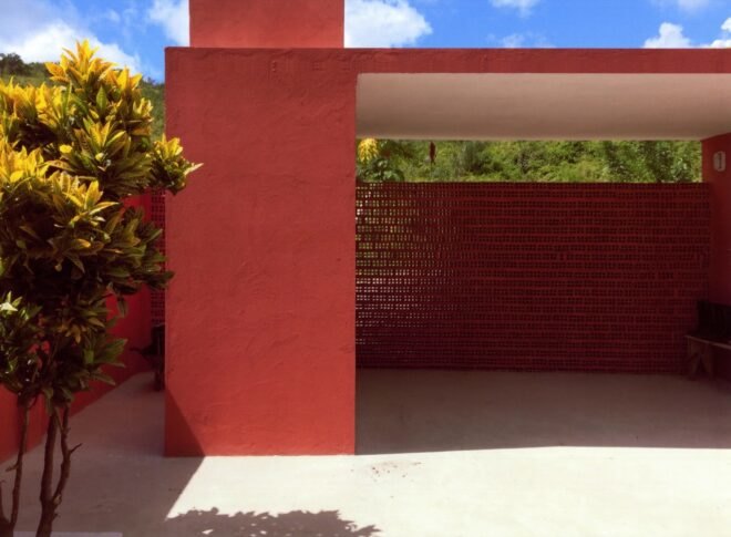to the left, a tree, to the right a red garage-like structure with dotted fence-like structure toward the back