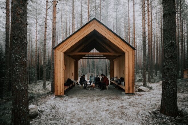 people huddled inside a gabled timber structure in a forest