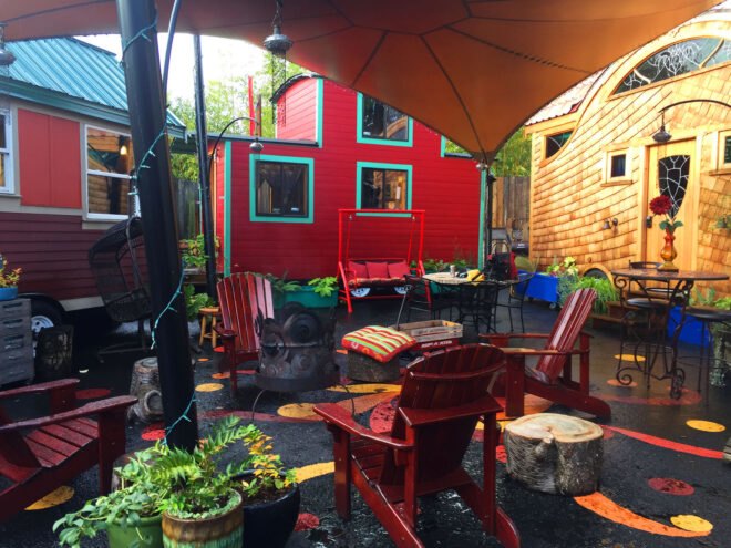 a small community area with red lawn chairs and an umbrella over the area. tiny houses surround the area