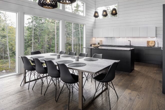 a kitchen with large windows on one wall. a dining table with chairs is set in the middle of the room.