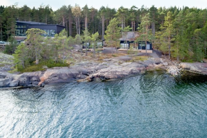 a blue body of water is surrounded by large rocks. on land, trees surround several house structures