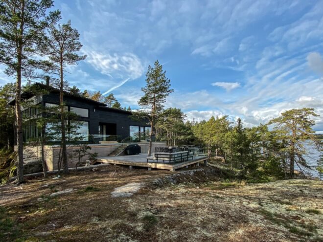 a landscape with trees and a body of water in the background. a house with patio and large windows sits to the left of the landscape