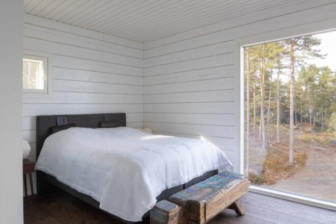 a white bedroom with one small window on one wall, and a large window on the opposite wall.