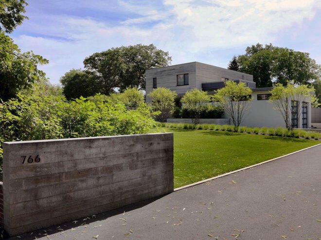 a side-view of a house, with greenery in the yard and a road leading up to the garage