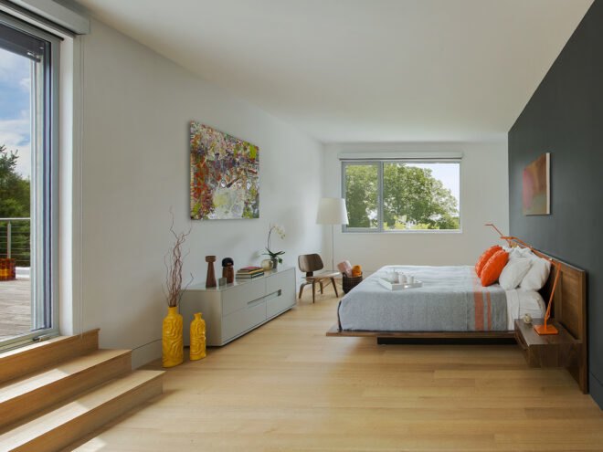 a bedroom with a dresser and yellow pots on the left, and a bed with orange pillows on the right