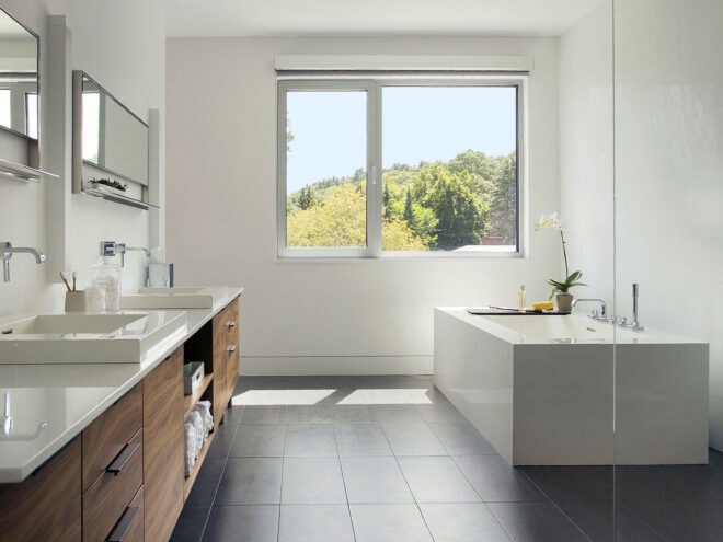 a bathroom with cabinets, sinks and mirrors on the left, a bathtub on the right and a large window on the opposite wall