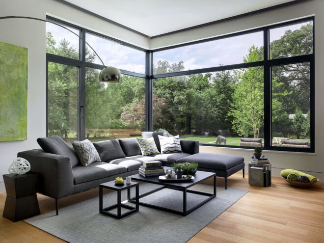 a living room with black sofas, two tables, a lamp and large floor-to-ceiling windows