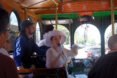 the interior of a trolley with two people guiding a tour at the front of the trolley. one tour guide wears a pink dress and hat, while the other person wears a suit and bowler hat