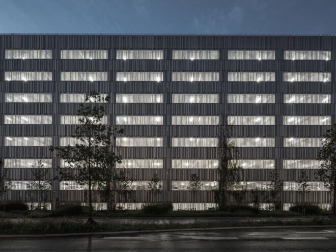 a night-time sideview of a silver, rectangular parking building