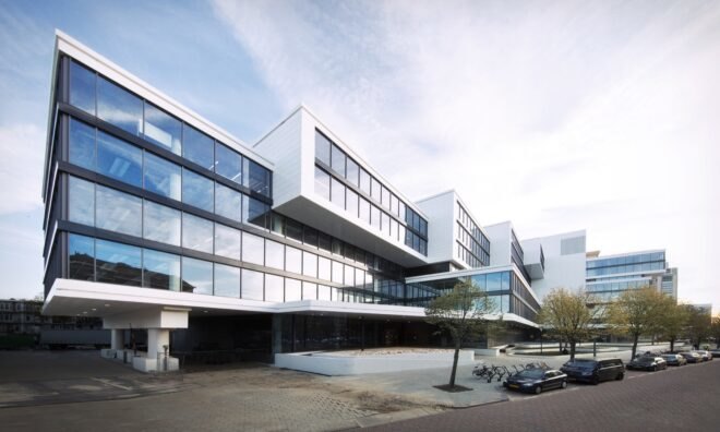 a tiered building with windows covering the facade and a cement courtyard in front