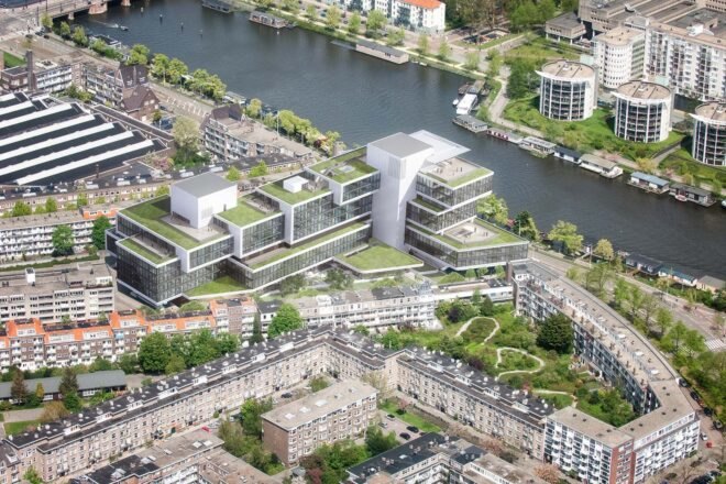 a bird's-eye view of the new Rivierstaete building, showing the city, trees and river. the new building features green rooftops
