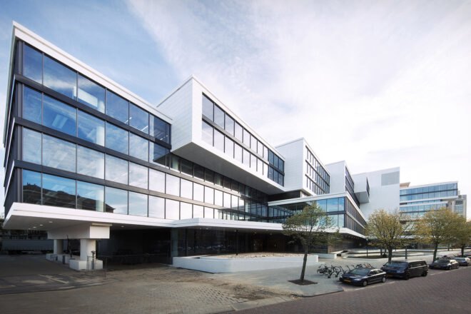 a tiered building with windows covering the facade and a cement courtyard in front