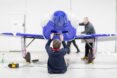 a person sits on the floor in front of a blue plane, taking a picture of it on a phone