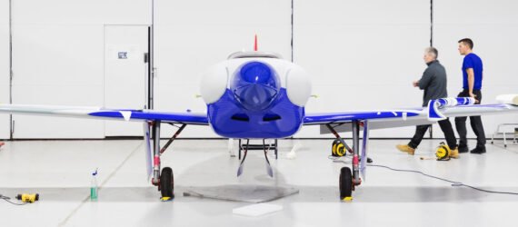 a photo of a small plane with blue detailing. two people walk by in the distance