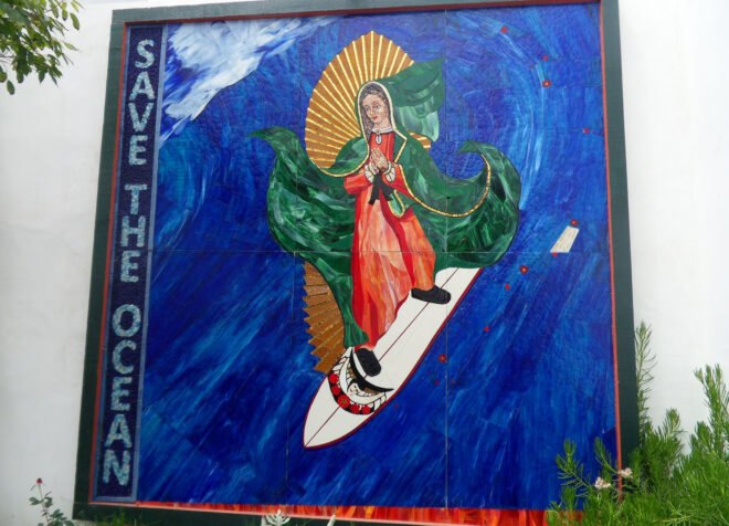 a square, blue mural with "Save the Ocean" written on the left and a religious figure riding a surfboard in the middle of the mural