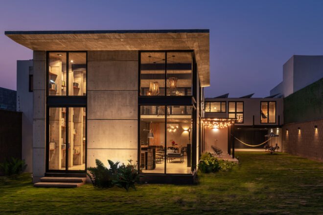 A large two story home in the evening time with light filtering out onto a green lawn