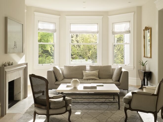 beige living room with beige sofa and two chairs near three windows