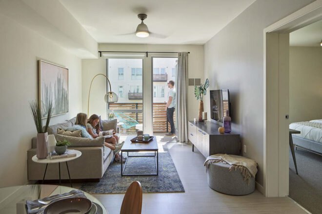 a living room with two children sitting on the sofa reading. the parallel wall shows a balcony that a person is standing on.