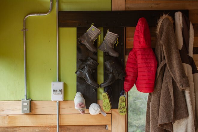 a green wall with a coat and shoe rack hung up, with pairs of boots and three coats hanging.