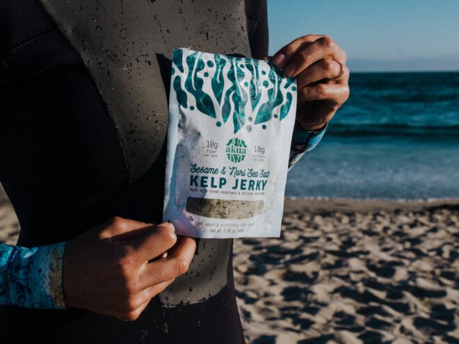 person on beach holding package of kelp jerky