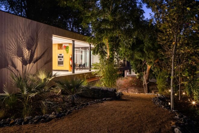 long, narrow wood home with large glass windows lit up at night