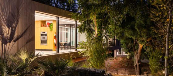 long, narrow wood home with large glass windows lit up at night