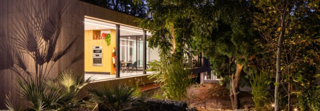 long, narrow wood home with large glass windows lit up at night