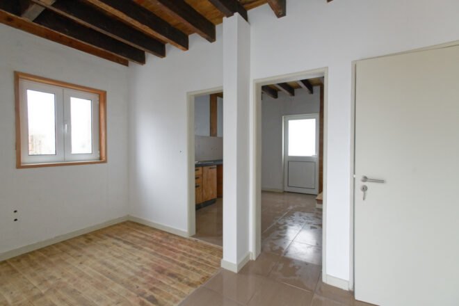 white room with two open doorways leading to other white rooms with wood ceiling beams
