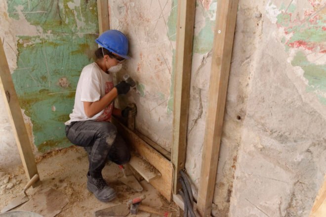person in hard hat adding insulation to old walls