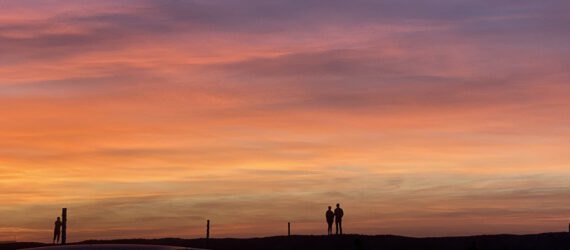 a shot of the horizon at sundown, with shadows of people in the distance