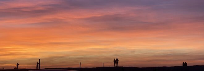 a shot of the horizon at sundown, with shadows of people in the distance