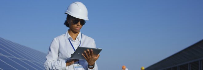 person working on a tablet and standing in front of solar panels