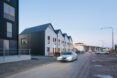 car driving past white and dark metal row homes