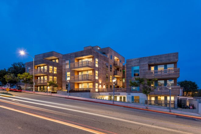 apartment complex clad in reclaimed timber lit from within at night