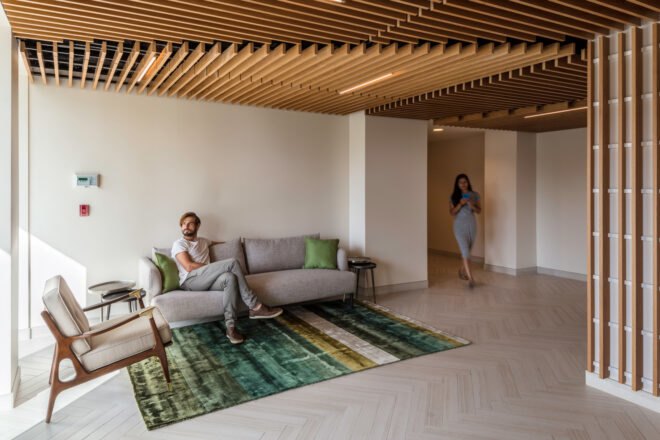 person sitting on gray sofa in apartment room with wood ceilings