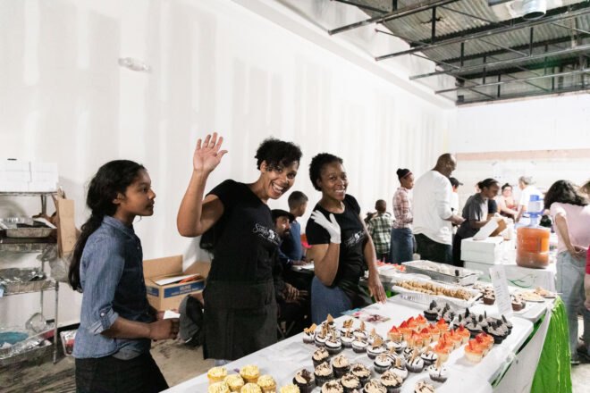 people waving while serving vegan cupcakes