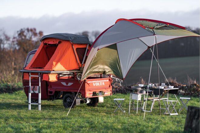 red vehicle with tent on top of it and extended tarp pulled out to the side