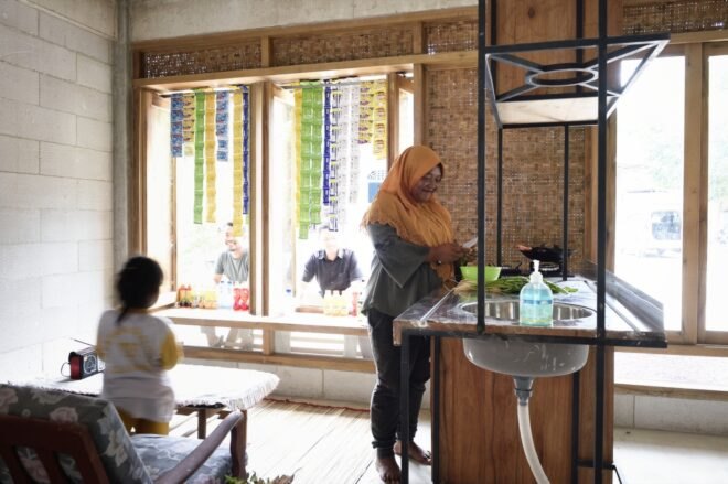 an adult cutting vegetables by the sink and a child standing near a coffee table looking out the window at two adults each sitting at separate windows.