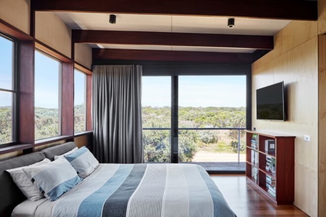 blue bed in large bedroom with wood ceiling beams and glass wall