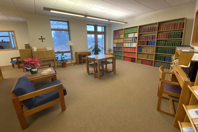 a library with colorful bookshelves, chairs, tables and windows.