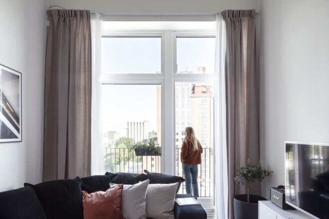person standing beside full-height window in an apartment