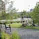 a green space with a walkway and bench and people lounging on the grass