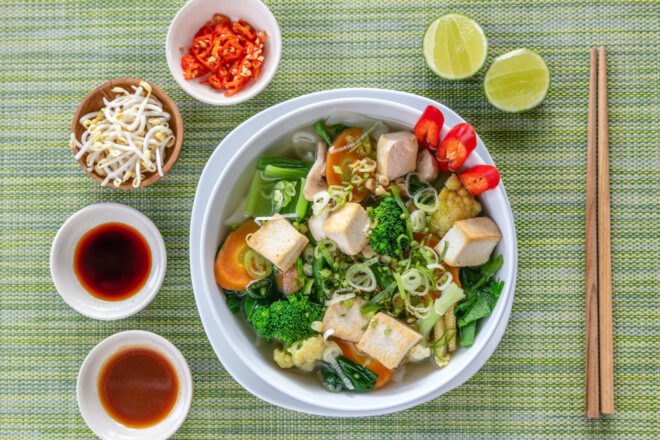 vegan pho and fresh toppings on a green background