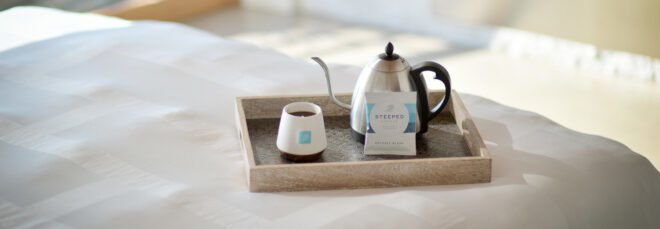 kettle, mug and package of a coffee bag on a tray on a hotel bed
