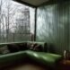 a green room with green walls and a green sofa. to the left is a floor-to-ceiling window that shows trees outside