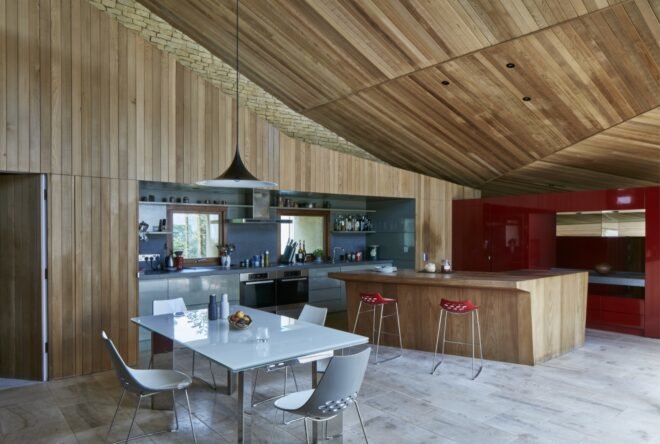 a kitchen area with wood walls and ceiling. to the right is a red wall. to the left, a white table and chairs.