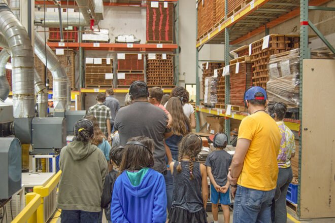 a group of children following an adult guide on a tour of a guitar factory